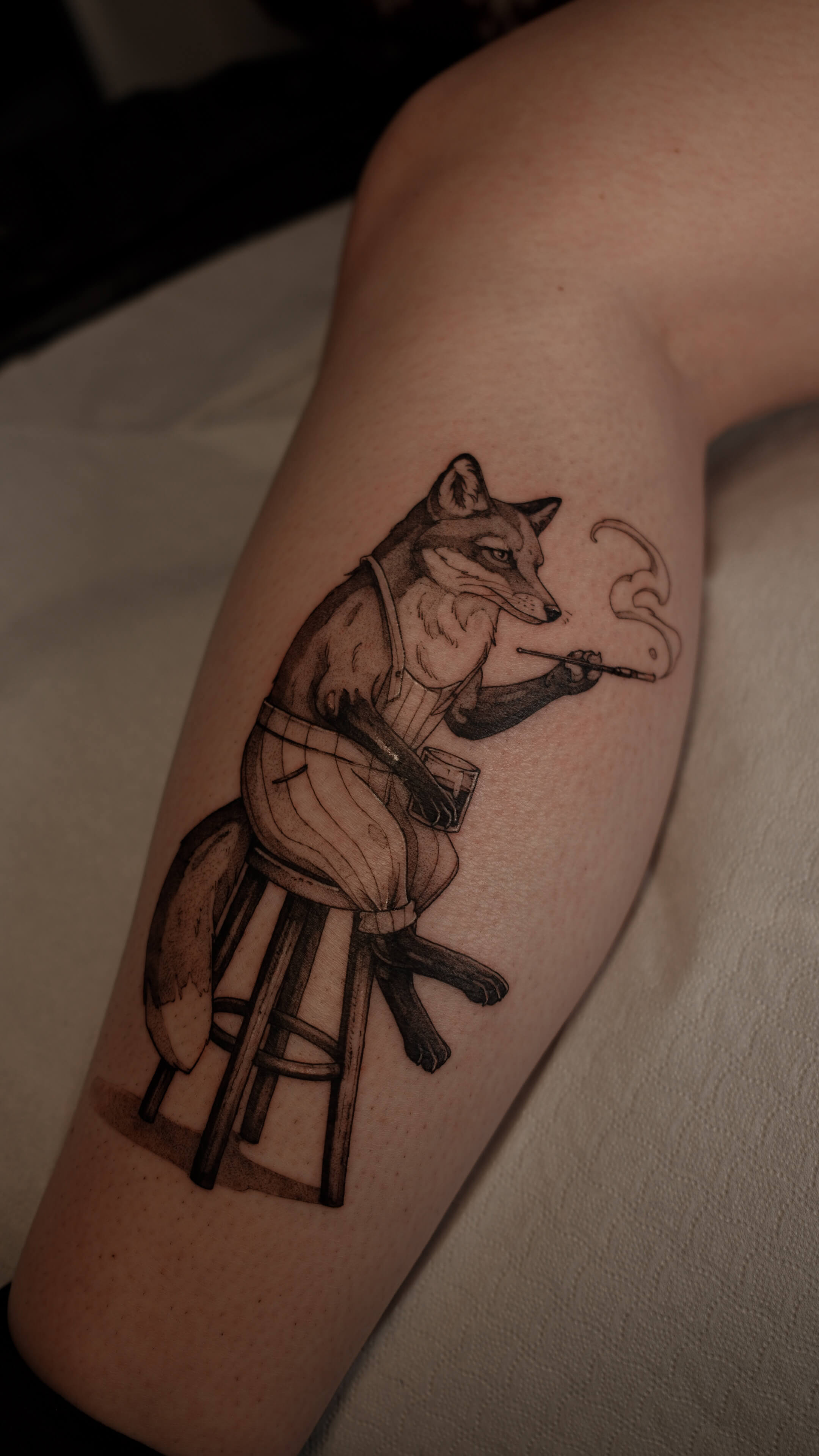 Graphic tattoo of a fox in waistcoat sitting and smoking on calf — tattoo Barcelona
